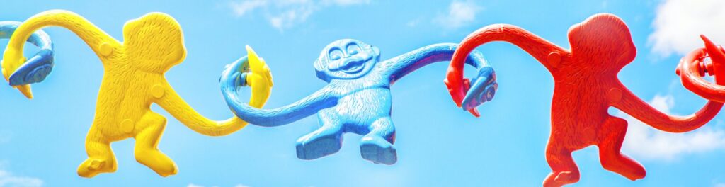 plastic monkeys (from a game) holding hands across a blue sky